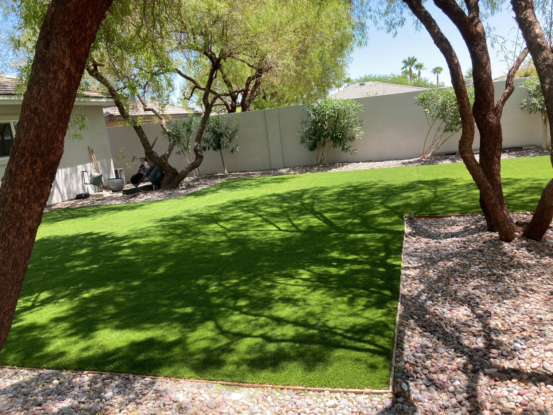 Shaded backyard turf installation bordered by river rock and mature trees