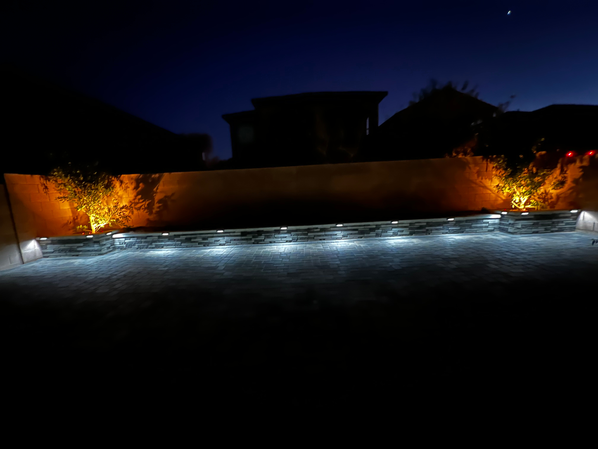 Night view of paver patio with wall lights and warm tree uplighting